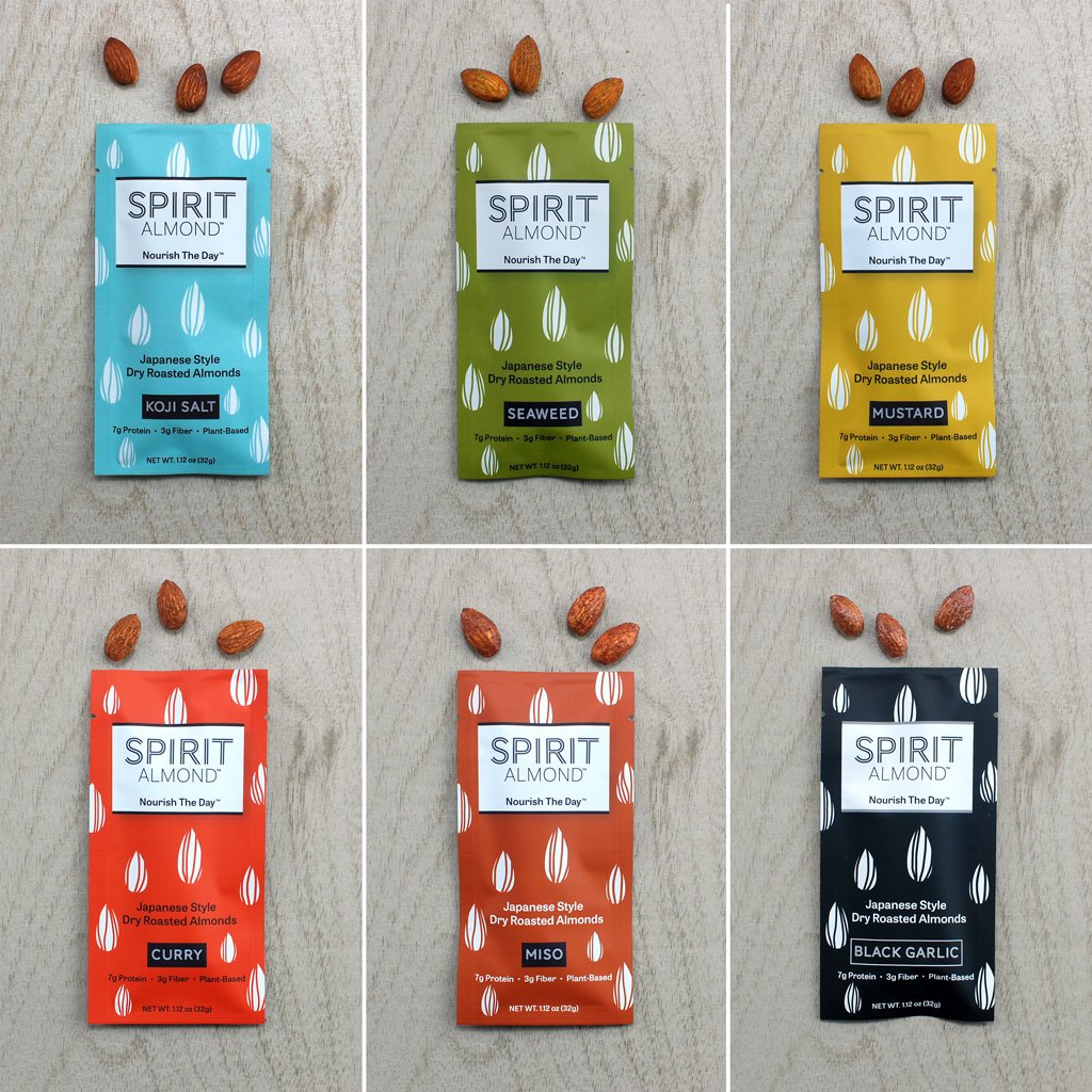 SPIRIT Almond Japanese Style Dry Roasted Almonds colorful lineup, six flavors.  Koji Salt, light blue. Seaweed, green. Mustard, yellow. Curry, reddish orange. Miso, brownish-red. Black Garlic, black. Each in 1.12 oz. single serving bags and a few almonds of each flavor above each bag.